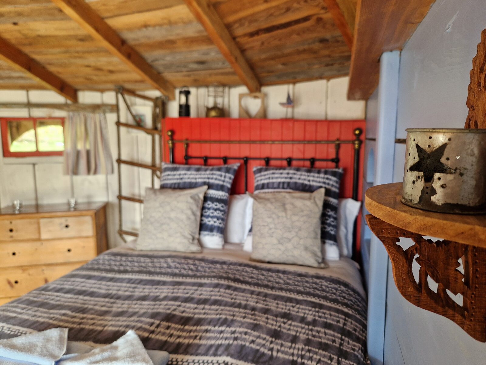 The double bed dressed with cushions, red headboard panel, and star candle holder on a carved wooden shelf