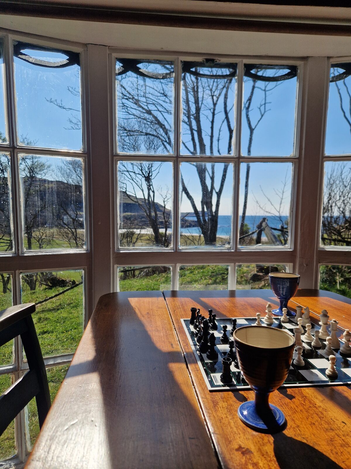 Dining table with chess set and goblet, bay view through the curved windows