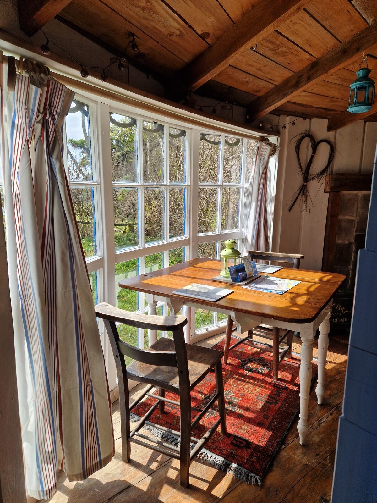 Sunlit dining area with striped curtains, heart decoration on the wall, and colourful rug