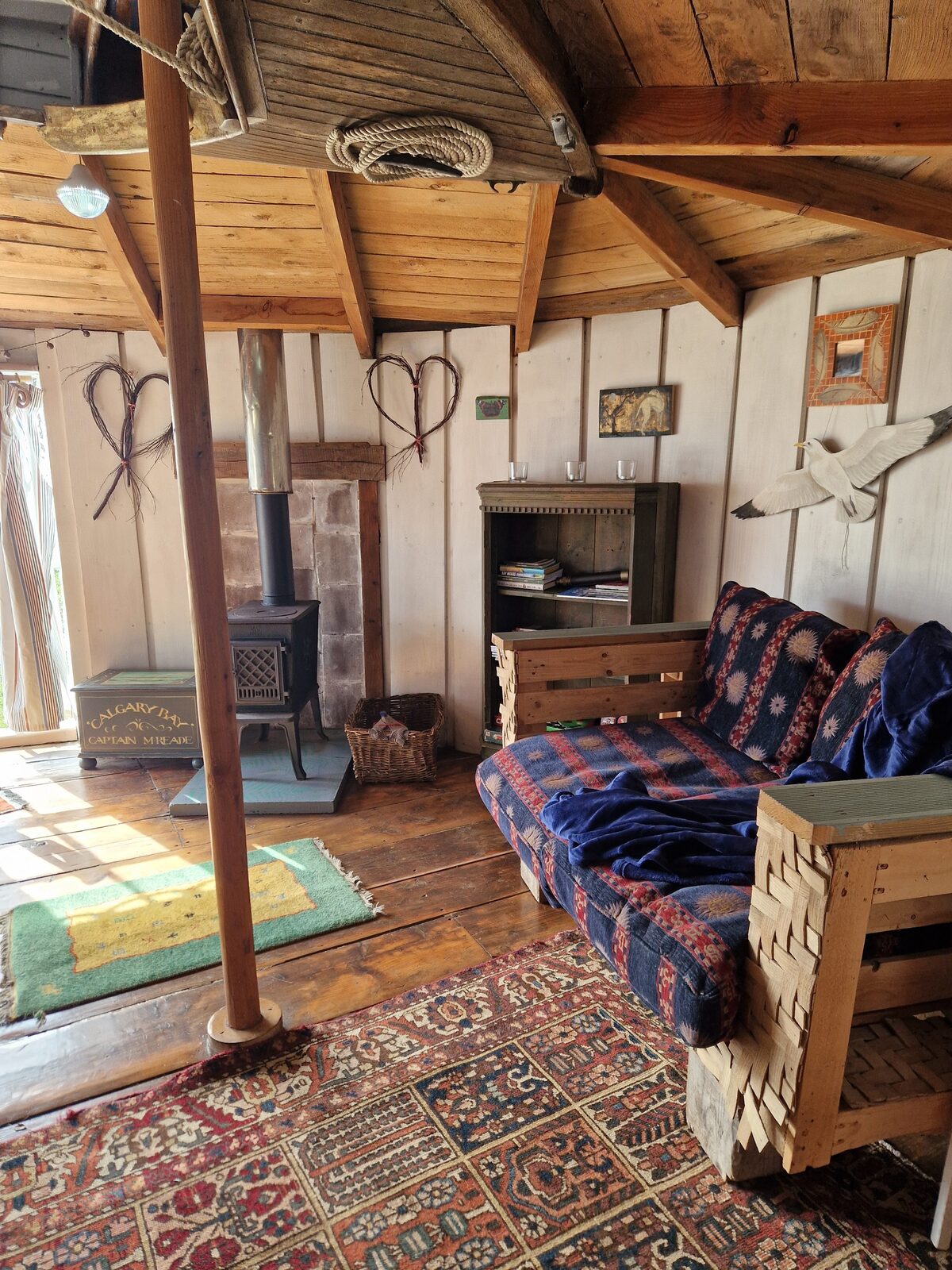 The living area — sofa with patterned throw, wood-burning stove, kittiwake sculpture on the wall, bookshelves
